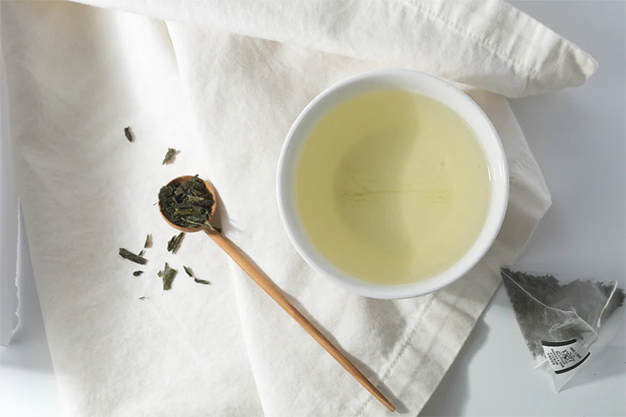 A bowl of green tea next to a spoon of green tea