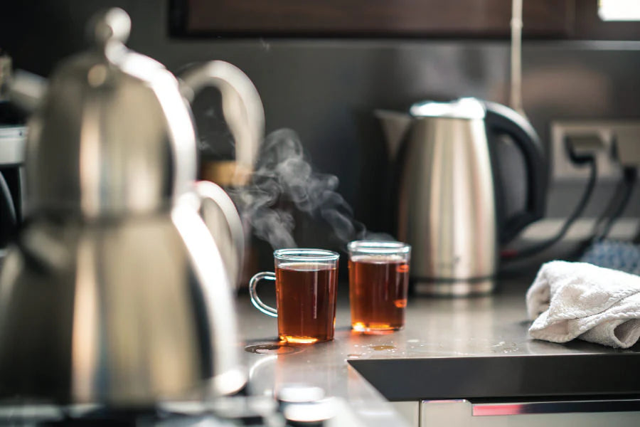 two glass cups of steaming tea a glass tea kettle full of brewed herbal tea